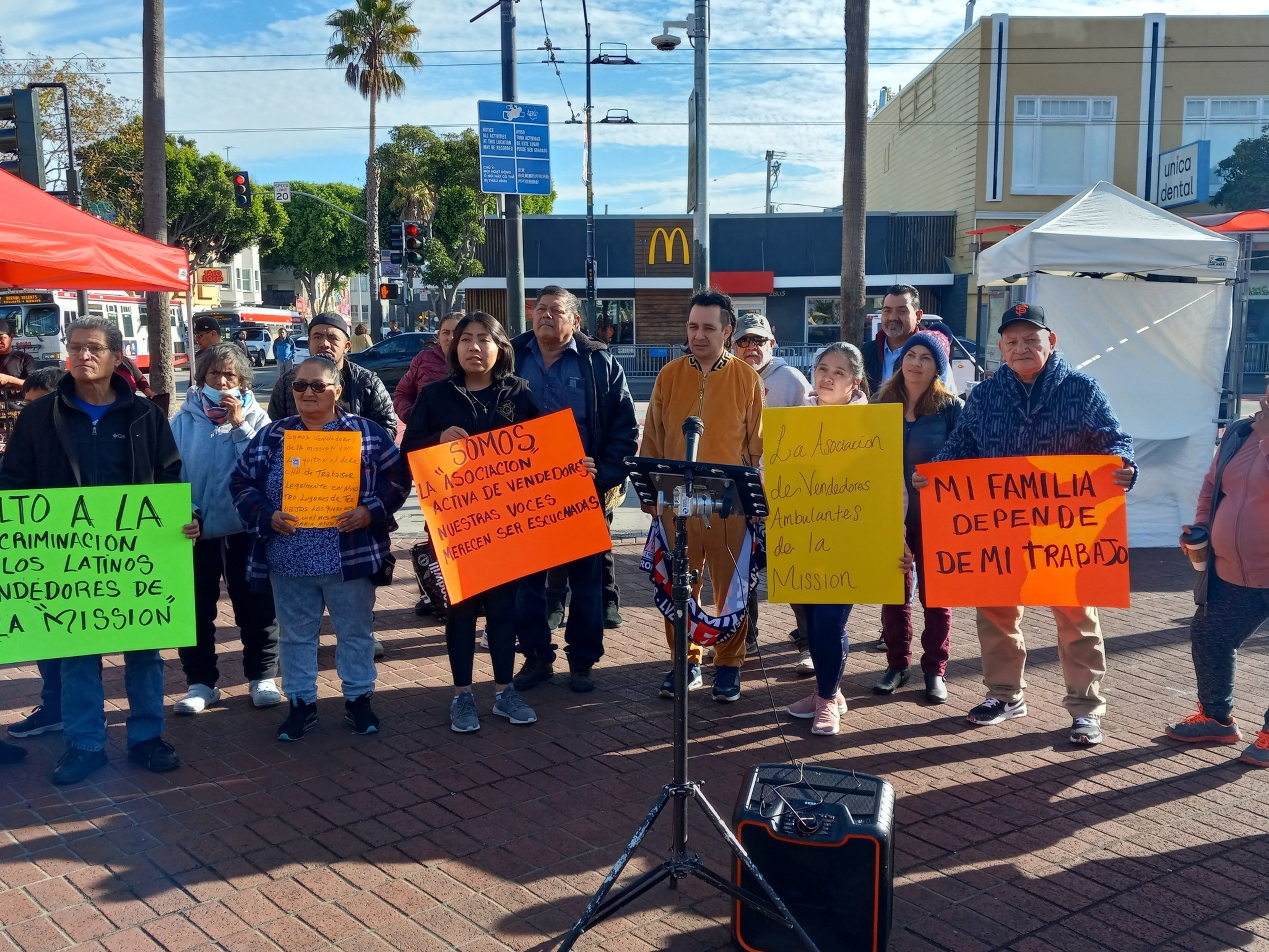A row of people holding neon signs protesting a proposed city ban on street vending.