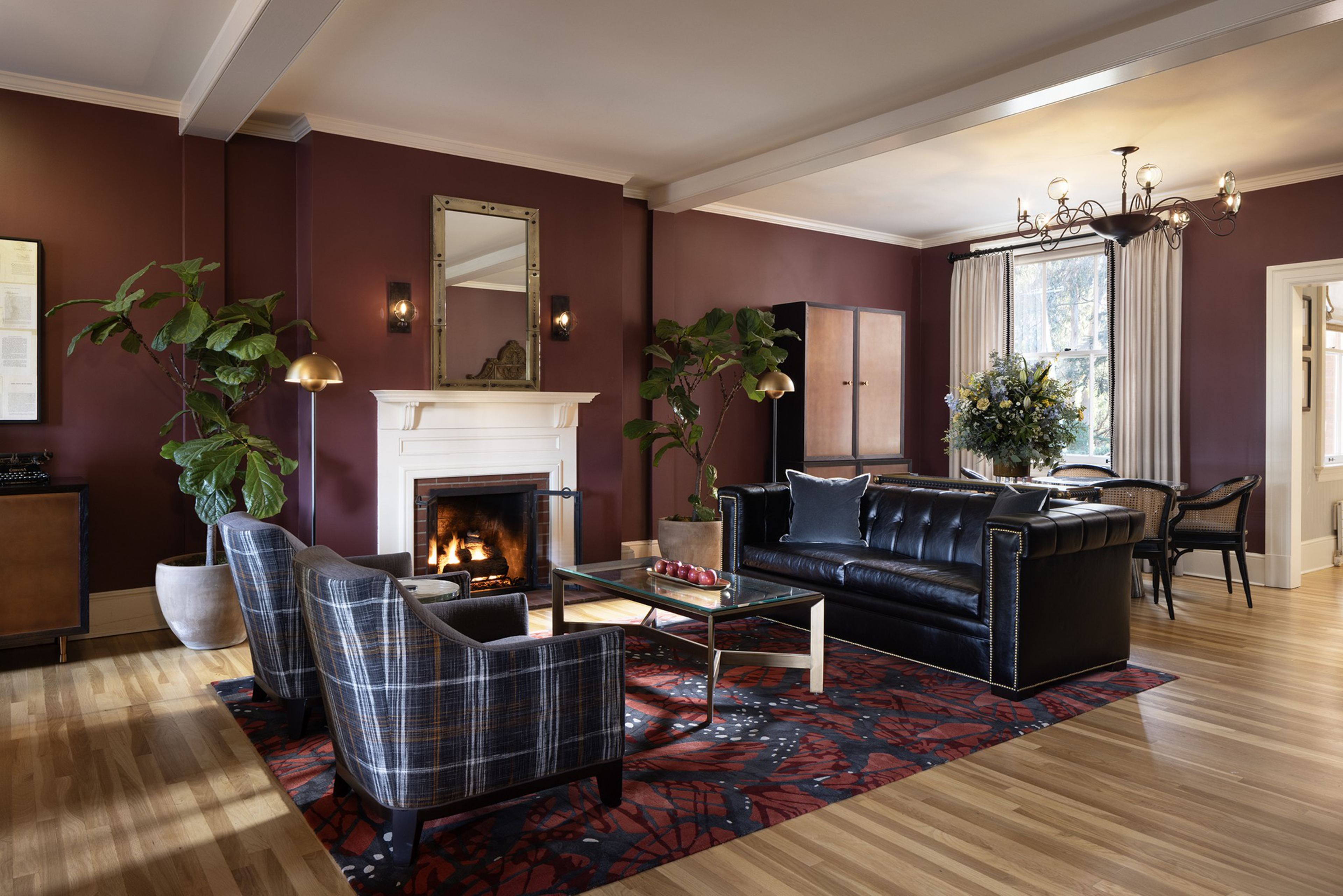 A room with dark red walls and gray and black furniture on a red and black rug and hardwood floor