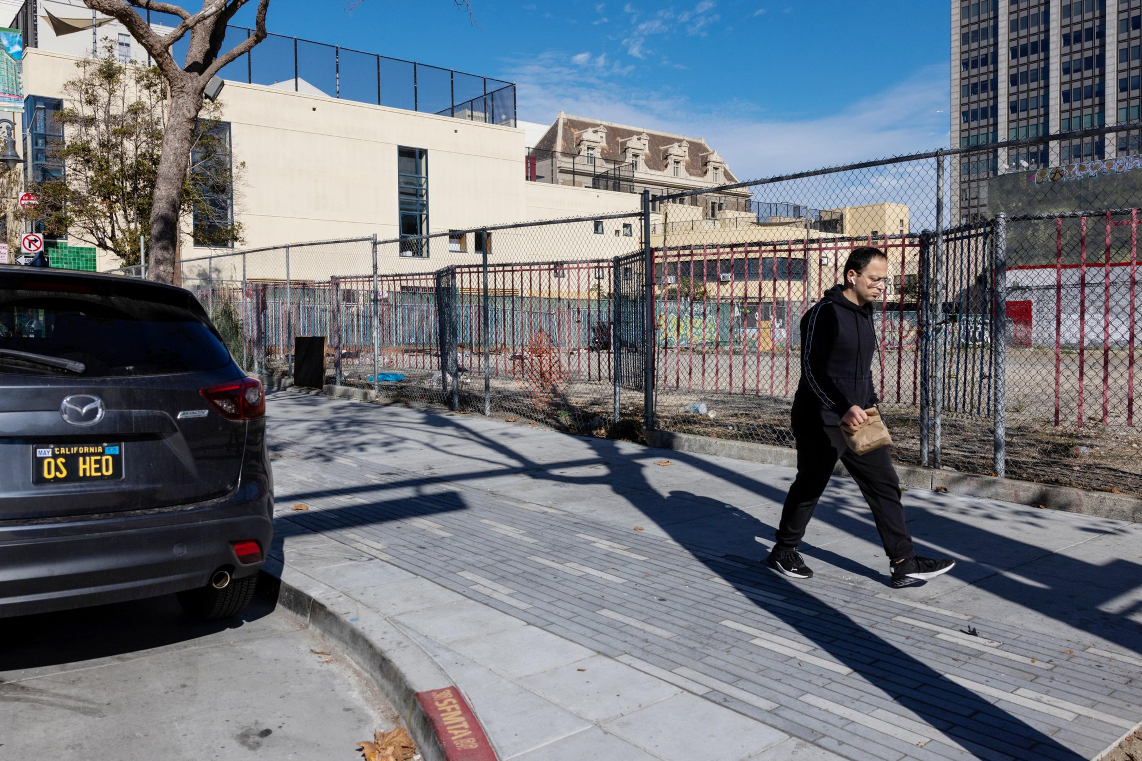 A pedestrian walks down the sidewalk with an empty lot in the background.