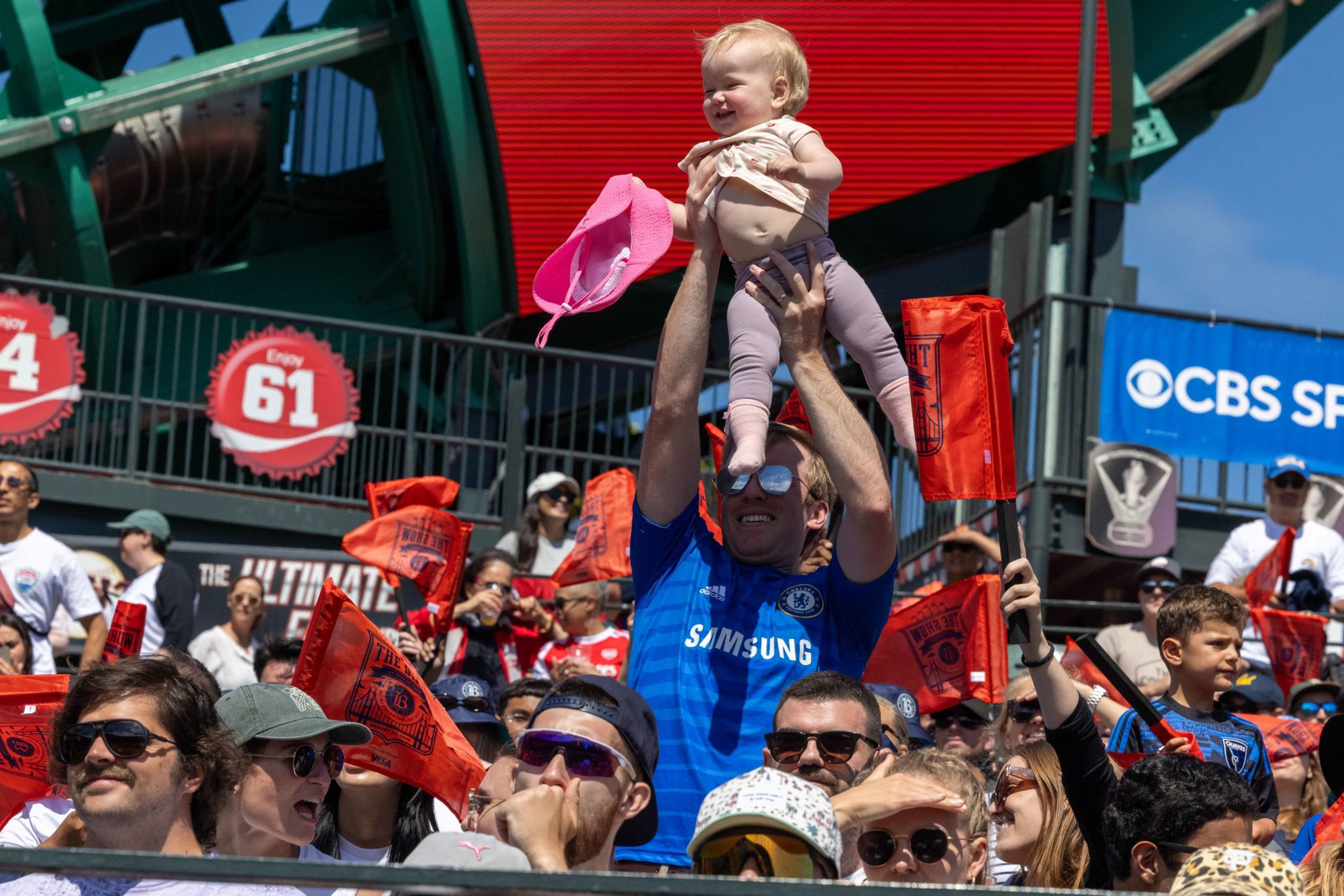 A man in a blue shirt holds a smiling baby above his head while a crowd of people around them wave red flags.