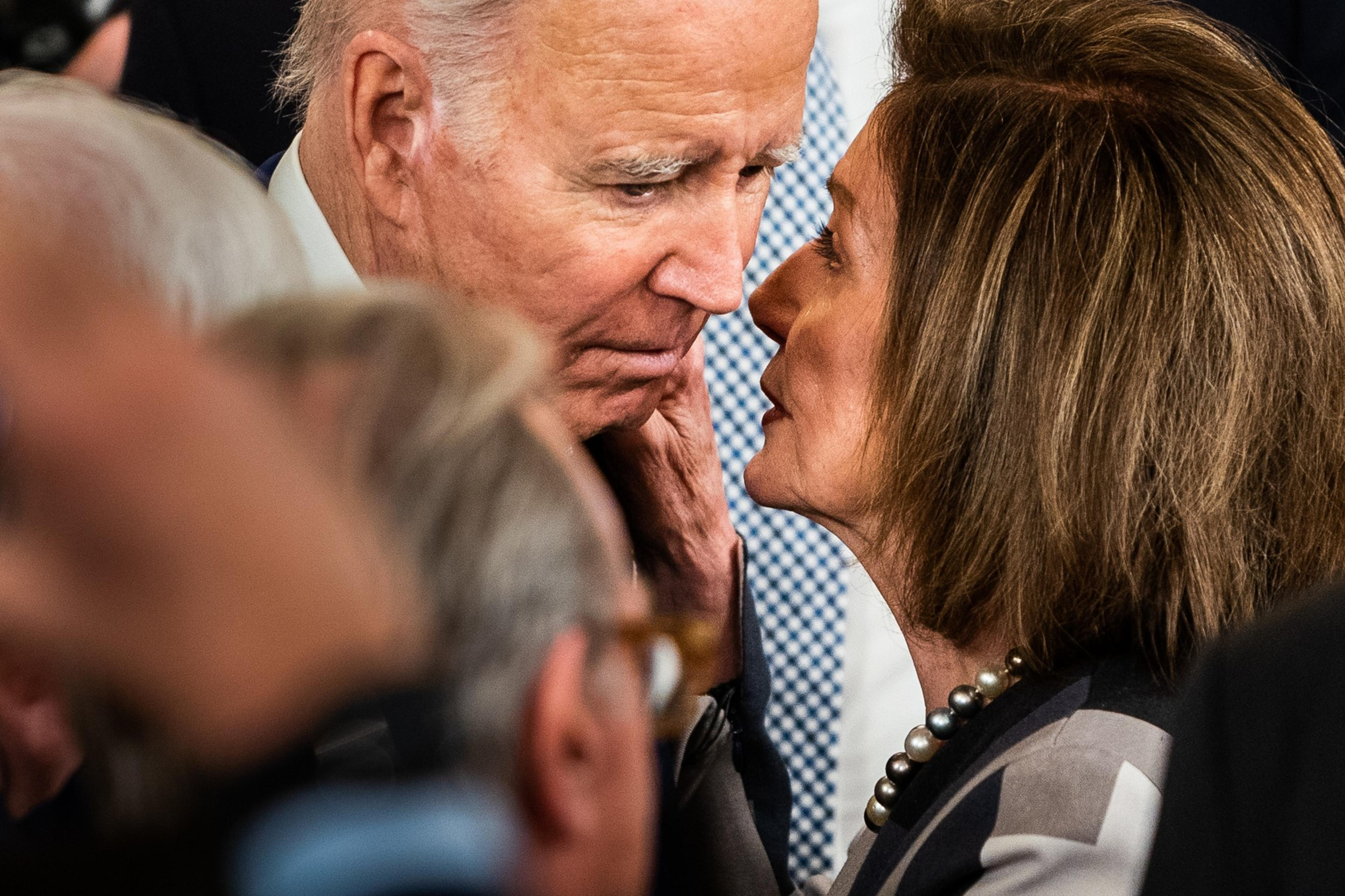 An elderly man and woman are engaging in a close, intense conversation amidst a blurred crowd. The woman's hands rest gently on the man's face.