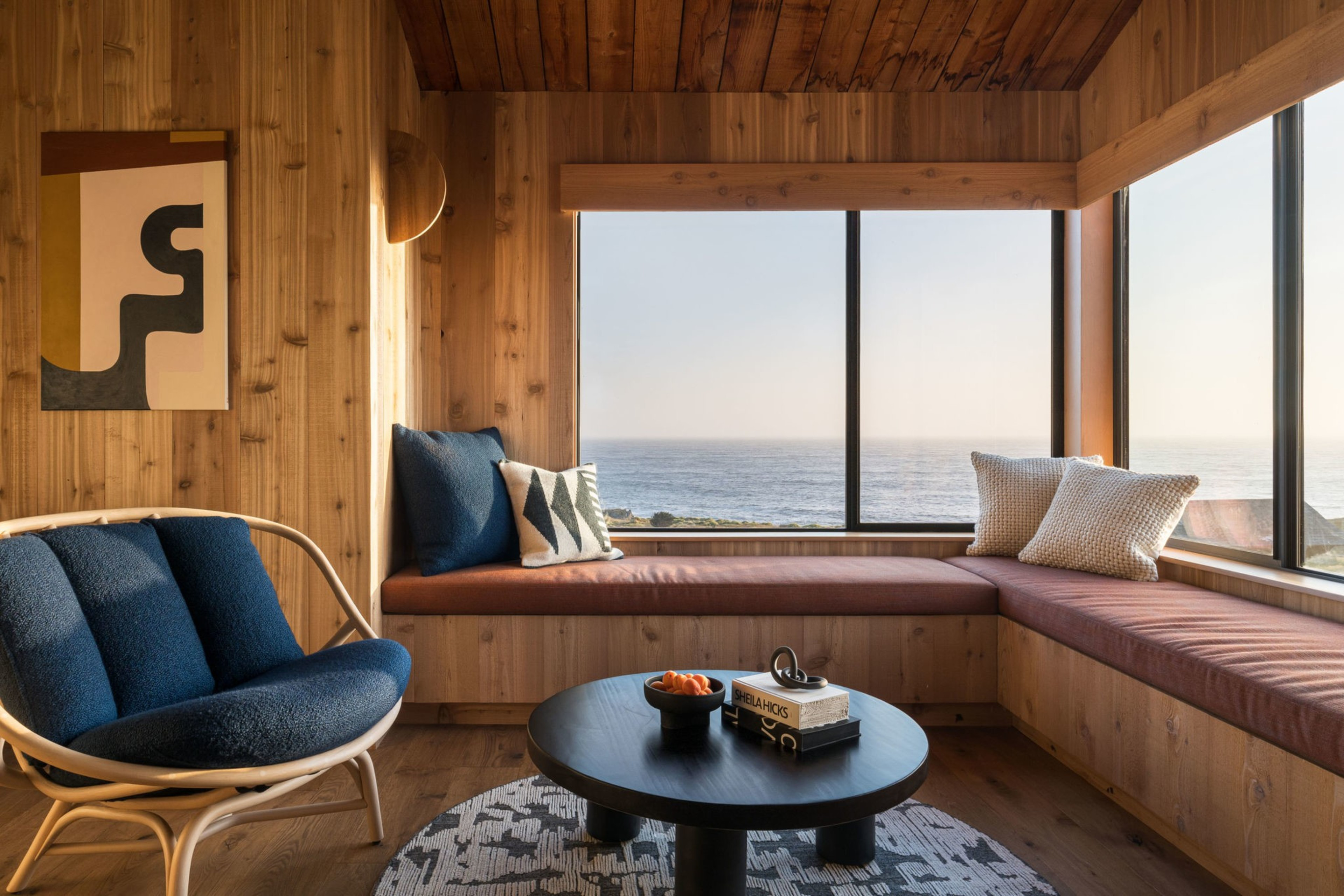 A wooden interior with large windows and long benches looks out on the ocean