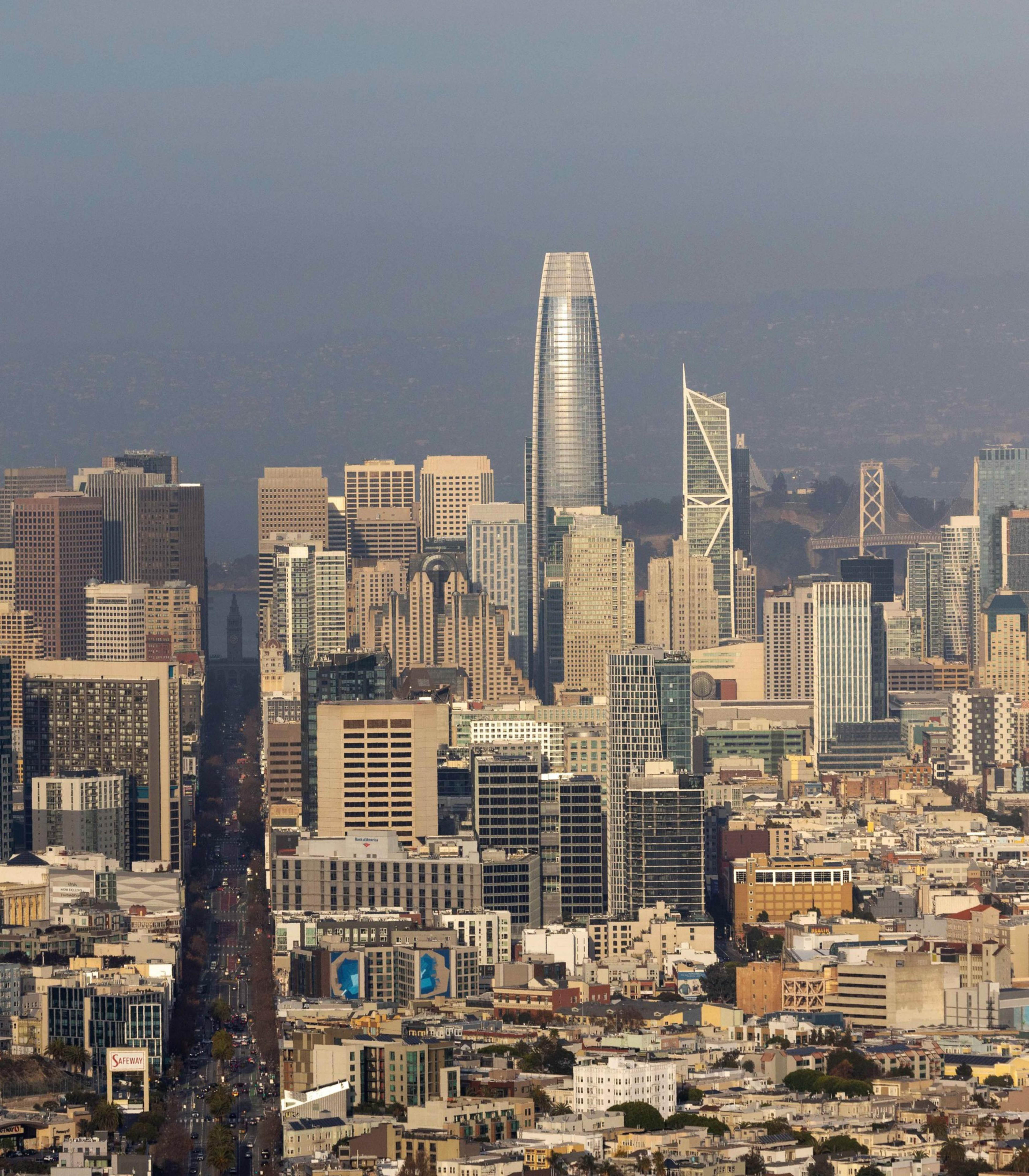 The image shows a dense cityscape with tall skyscrapers, including a shiny, cylindrical tower. Streets and lower buildings are visible in the foreground.