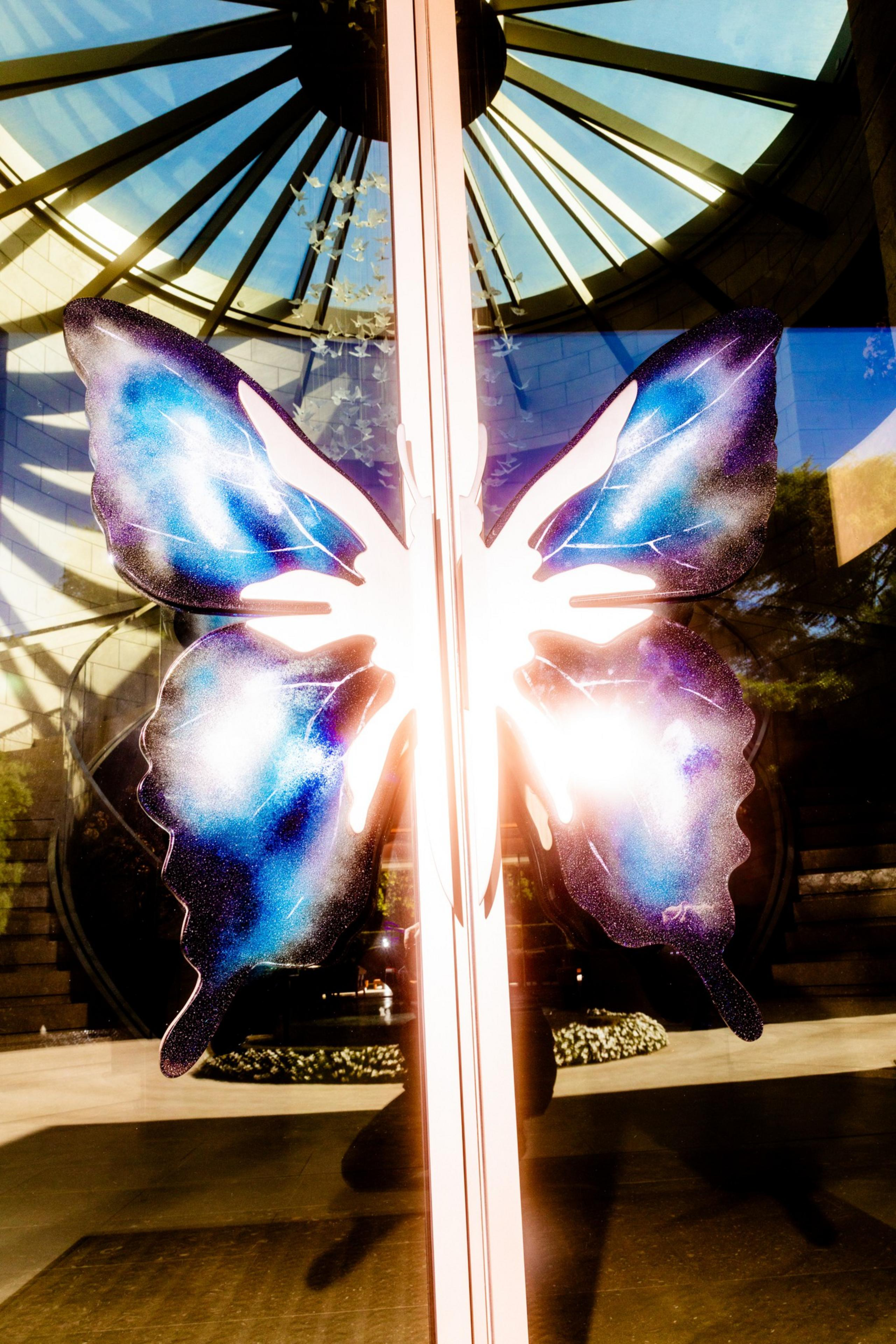 A large, colorful butterfly decal in blue and purple is displayed on glass doors, reflecting a circular skylight and outdoor surroundings.