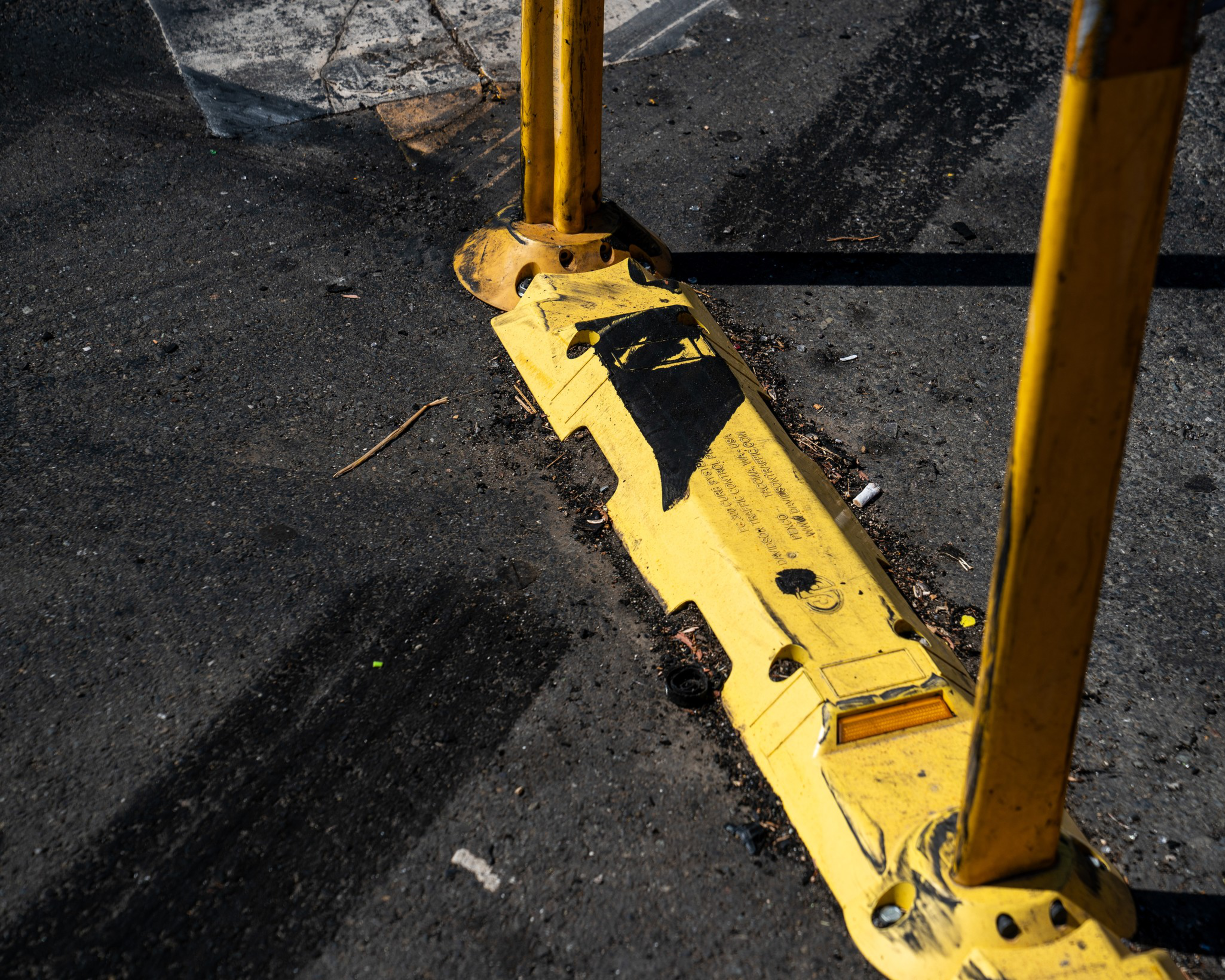A close-up of a worn yellow traffic barrier set on asphalt, with visible black tire marks and debris scattered around.