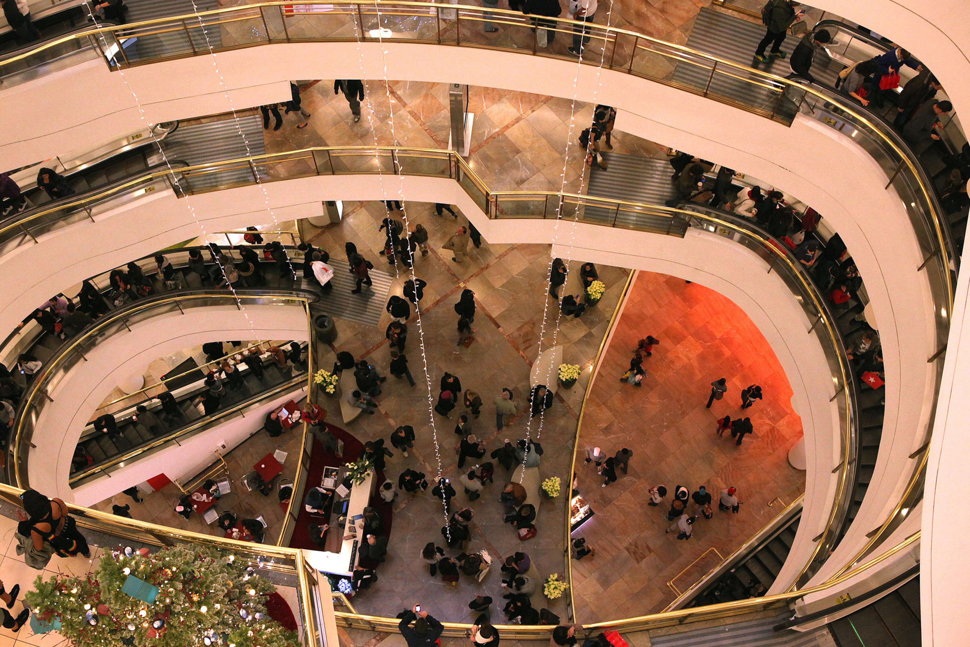 An indoor multi-level shopping mall with shoppers and curved escalators.