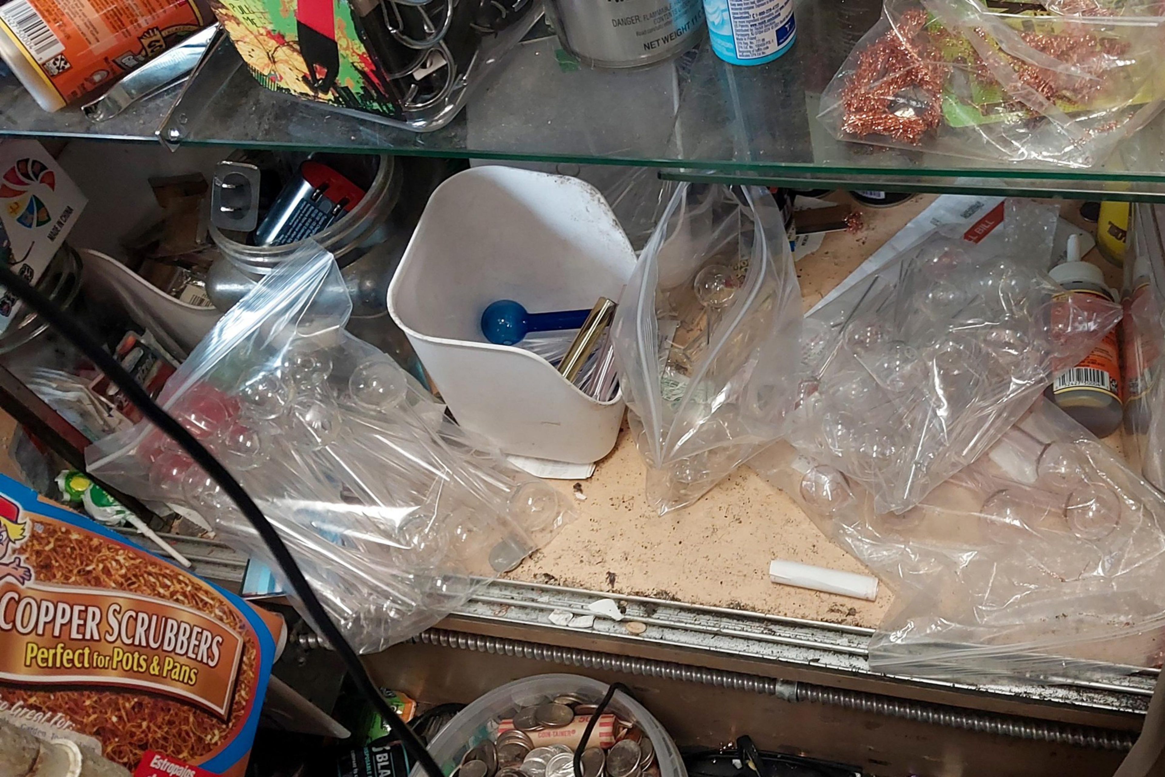 The image shows a cluttered shelf with various items, including batteries, copper scrubbers, plastic bags, and a container with a blue scoop.