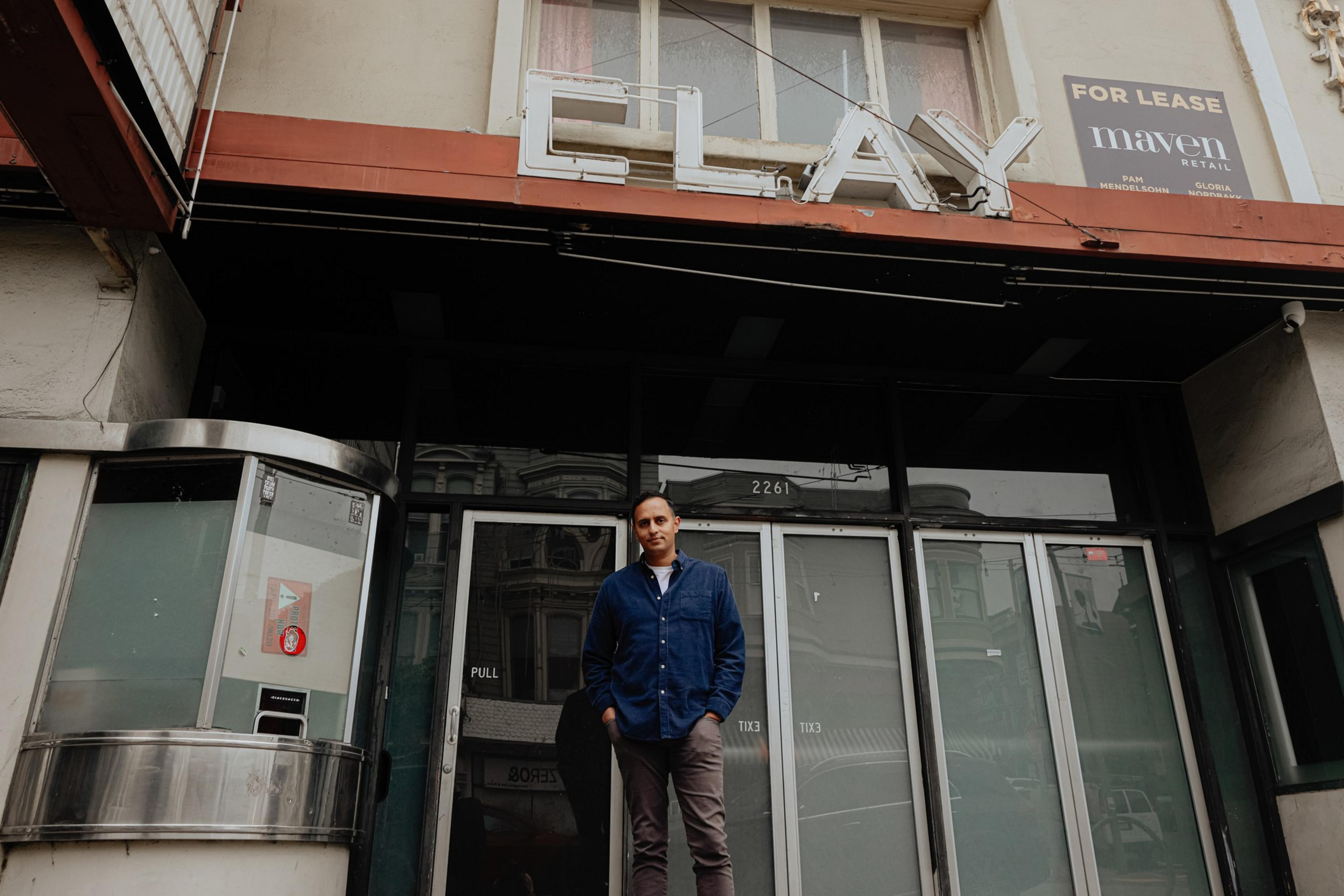A person stands in front of a closed building with a sign reading &quot;CLAY&quot; above the door. A &quot;For Lease&quot; sign is visible, and there's an old ticket booth nearby.