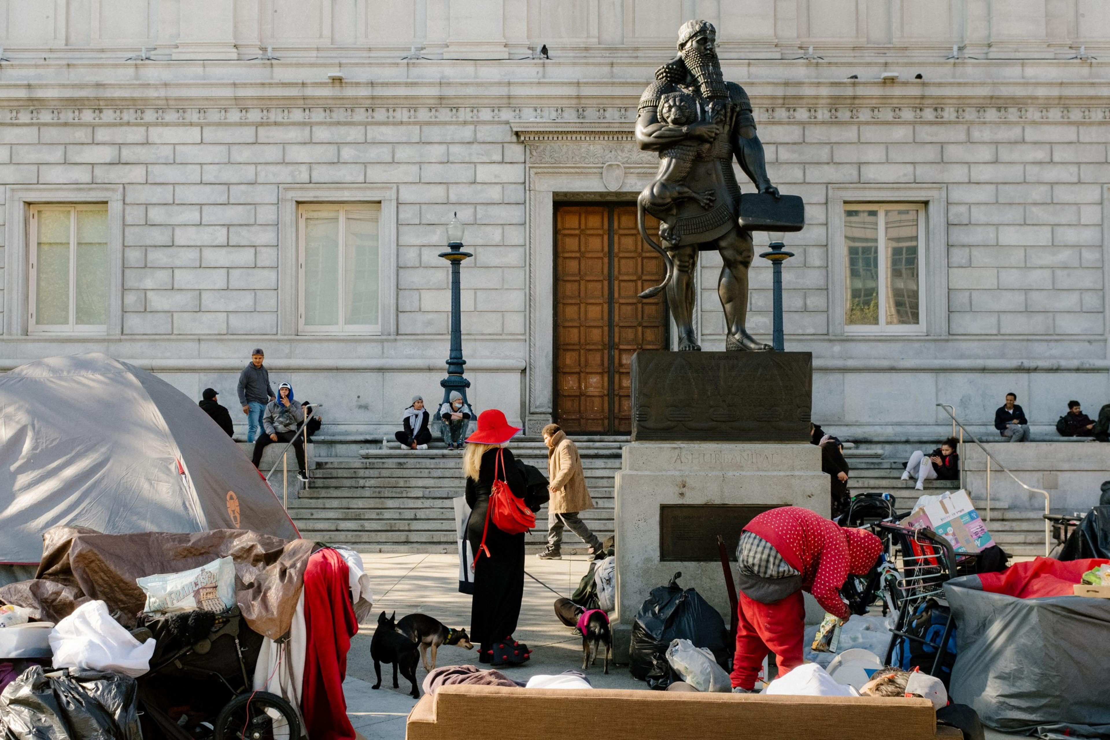 People linger around a courtyard area that has a large statue of a standing bearded man on a pedestal.