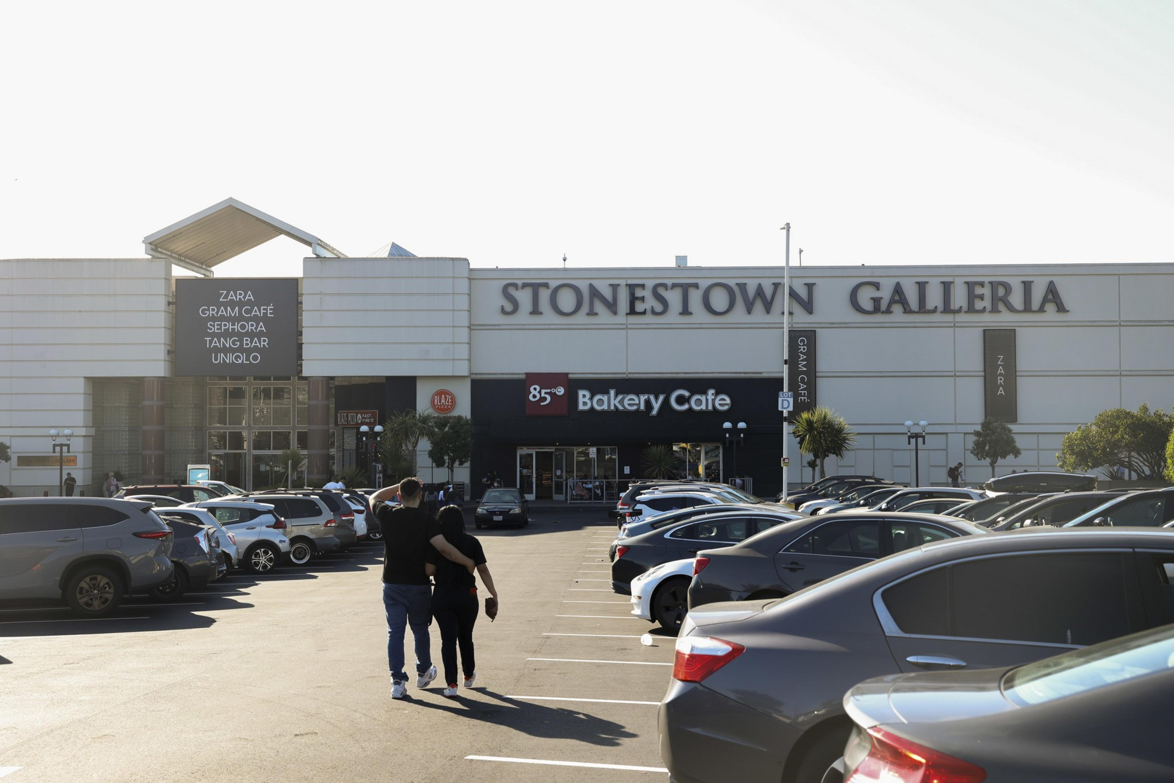 People walk through a parking lot outside a mall.