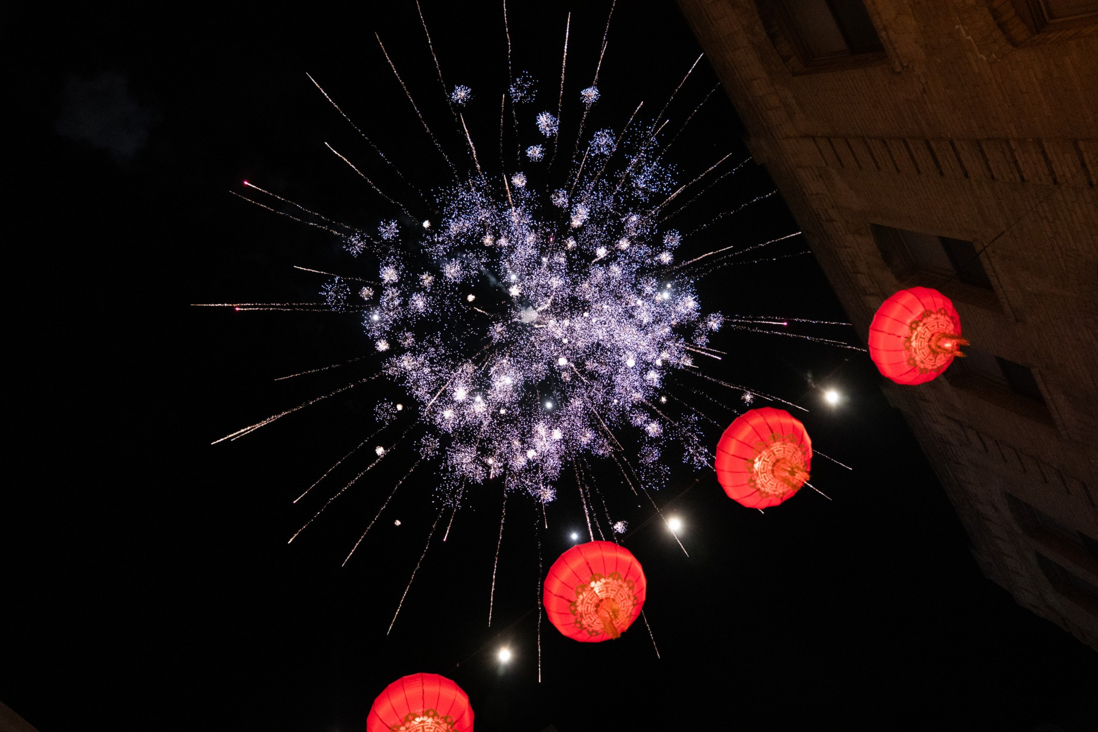 Bright purple fireworks explode in the night sky above a building ...