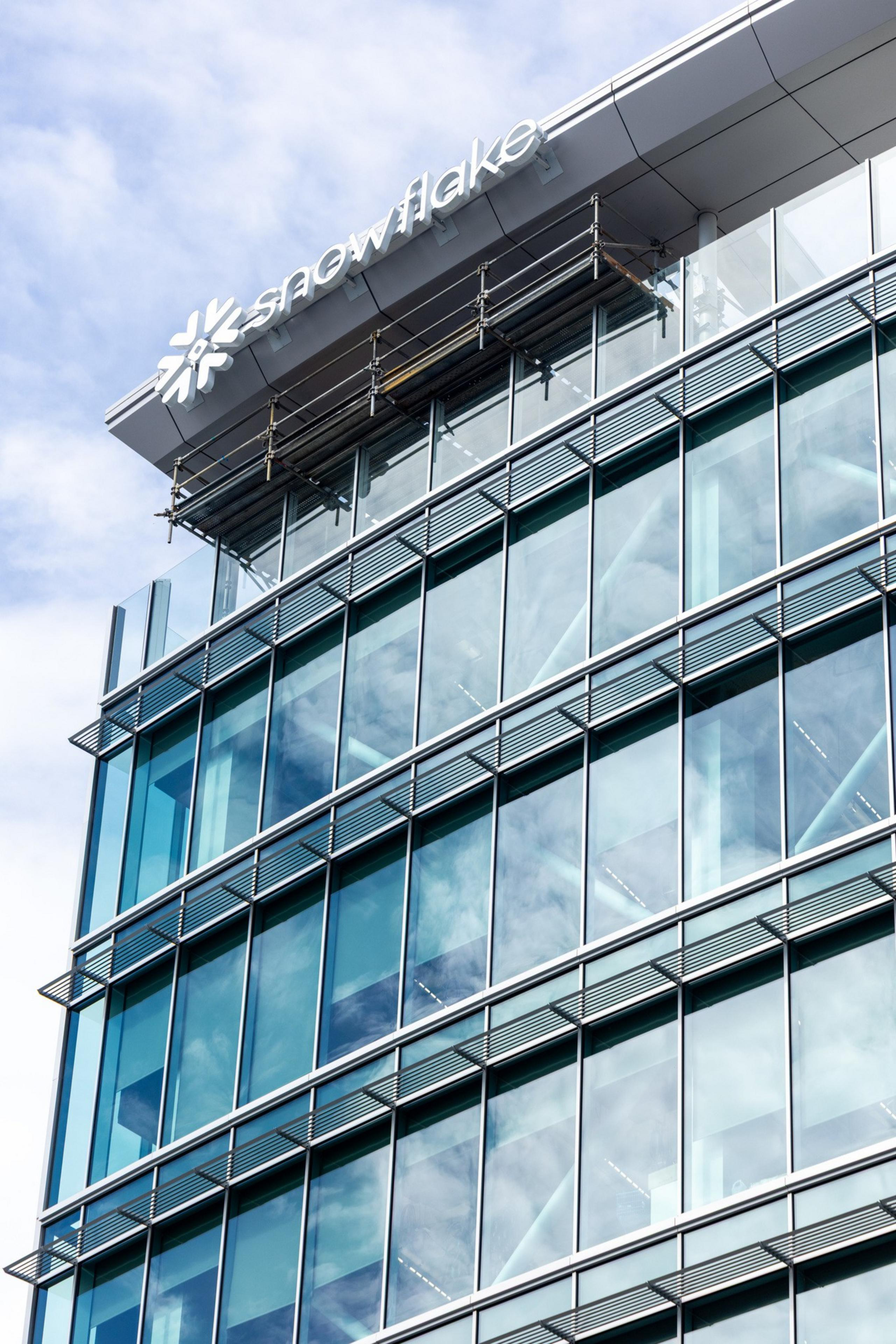 A modern glass office building with reflective windows shows the "Snowflake" logo and name at the top against a partly cloudy sky.